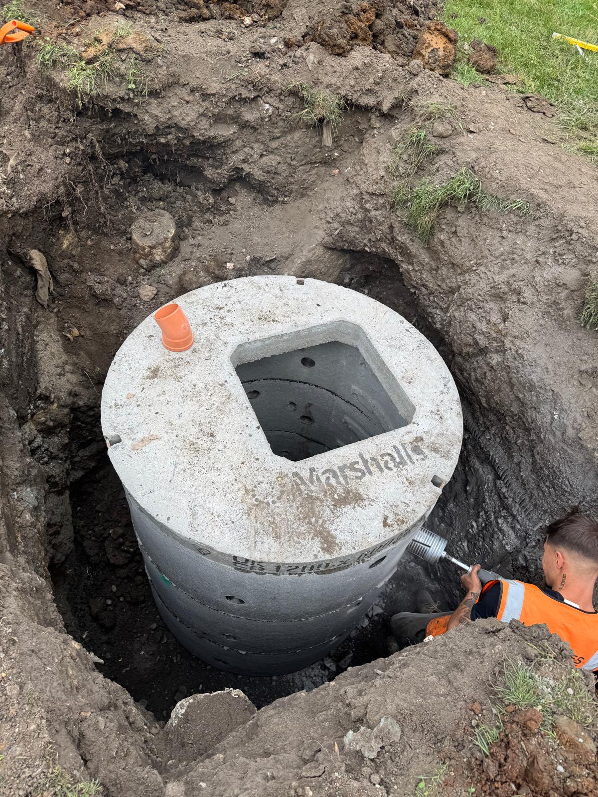 Worker installing large cylindrical concrete drainage chamber